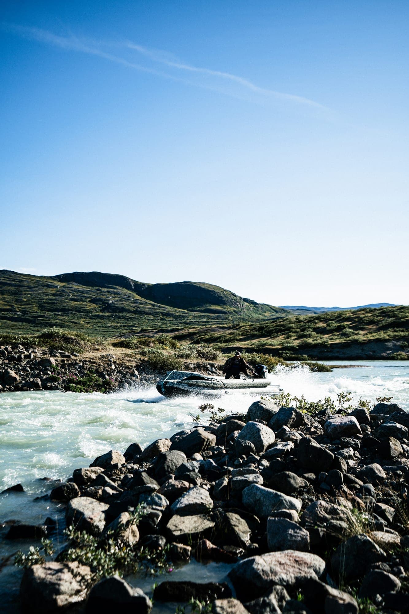 Rapids in a river below green hills
