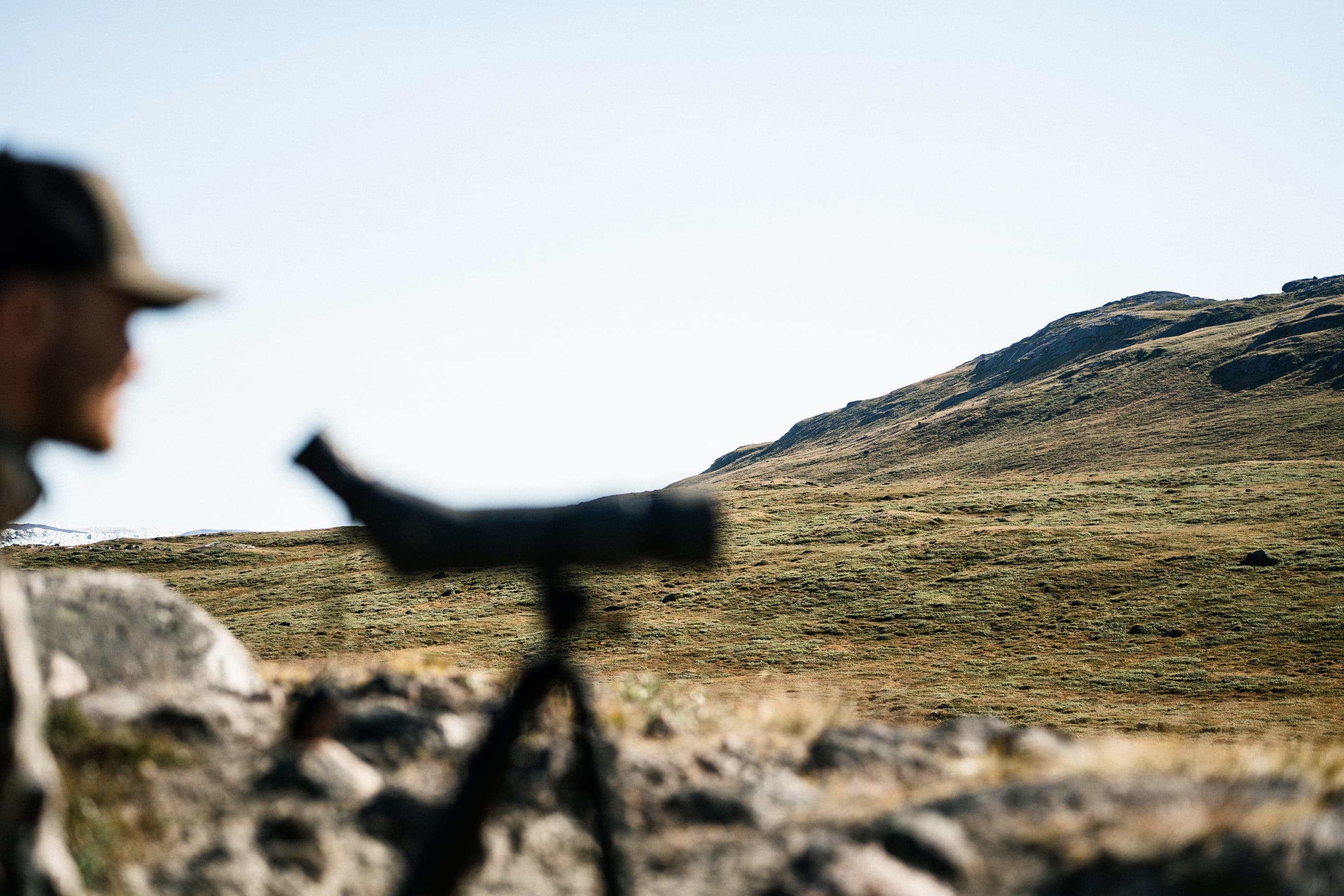 A spotting scope on a tripod aimed at the slope, the guide out of focus at the edge