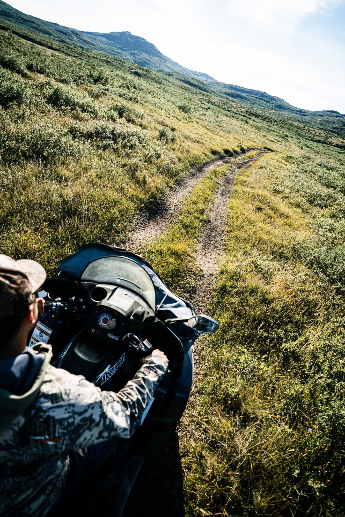 A guide on an ATV seen from behind, on a track across the tundra