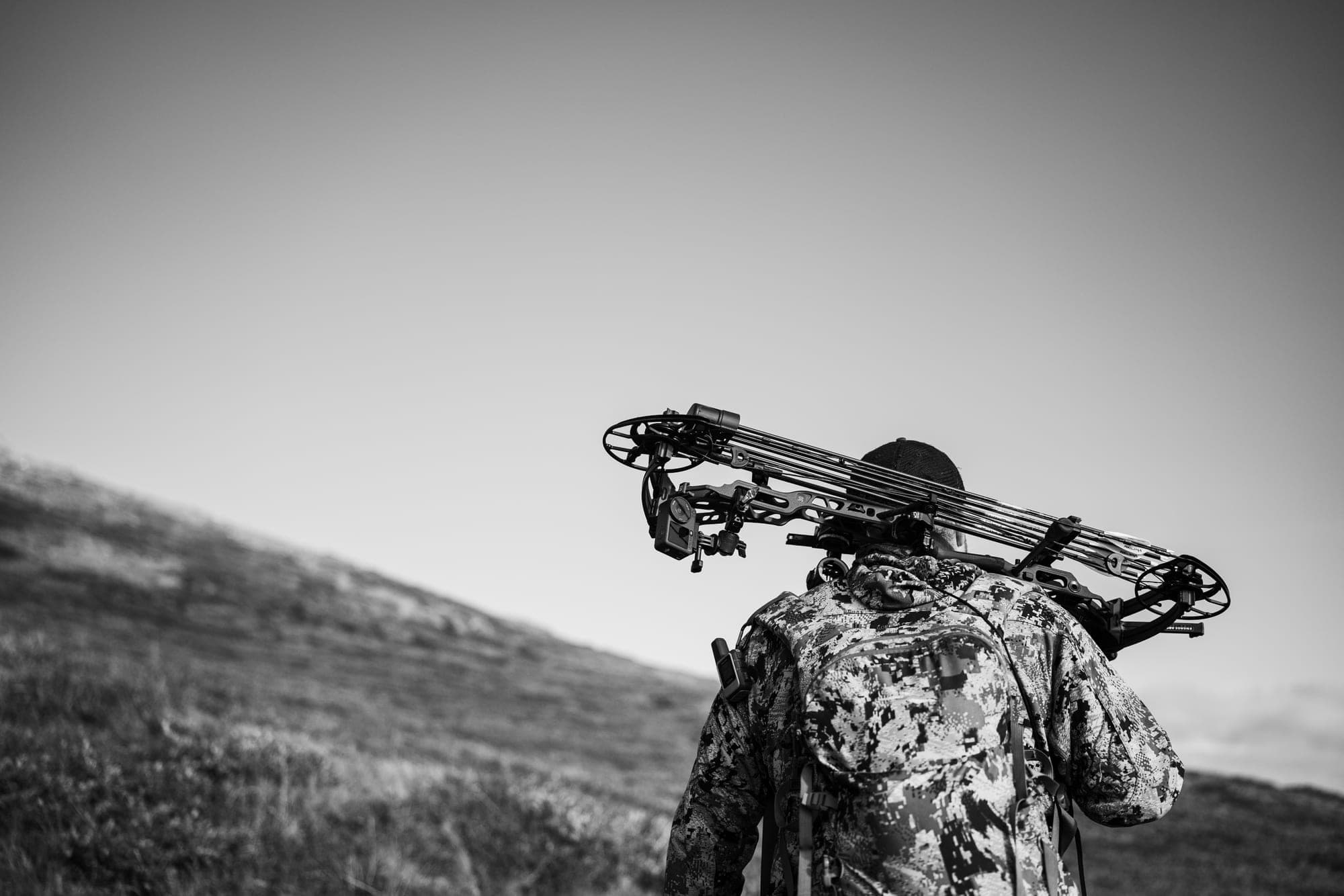 A bowhunter seen from behind with a bow over one shoulder, in black and white